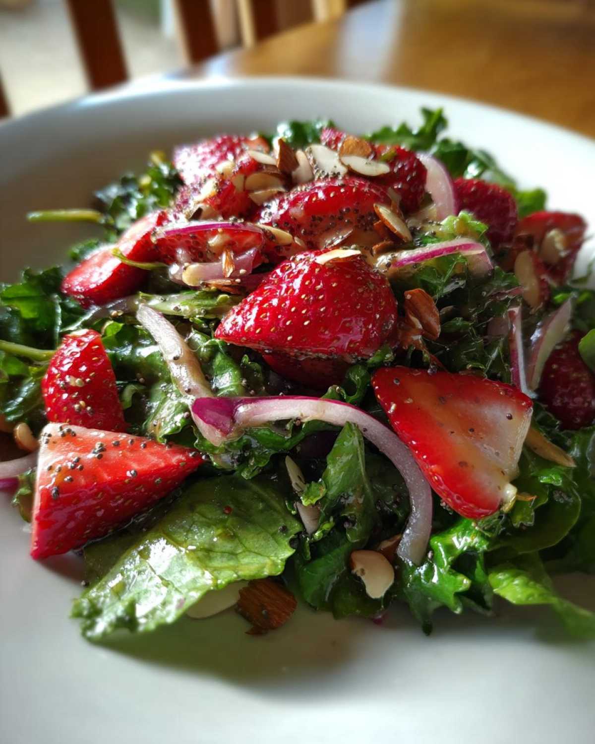 A vibrant close-up of Strawberry Spinach Salad featuring sliced strawberries, red onion, almonds, and poppy seeds.