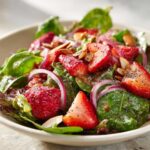 Close-up of a vibrant Strawberry Spinach Salad with sliced strawberries, red onion, almonds, and poppy seed dressing.