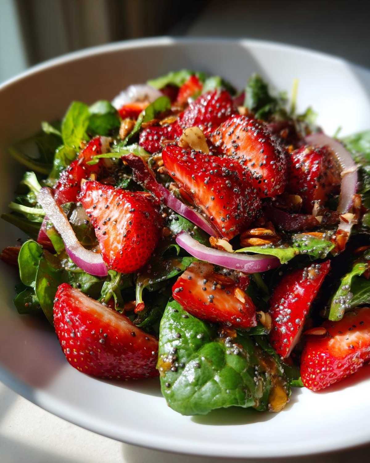 Close-up of a vibrant Strawberry Spinach Salad with poppy seed dressing, red onion, and nuts.