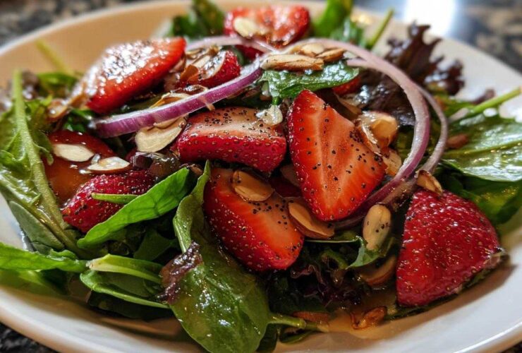 Close-up of a vibrant Strawberry Spinach Salad with sliced strawberries, red onion, and almonds, coated in dressing.