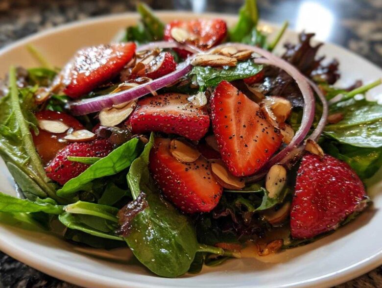 Close-up of a vibrant Strawberry Spinach Salad with sliced strawberries, red onion, and almonds, coated in dressing.