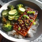 Close-up of a Teriyaki Salmon Rice Bowls serving featuring glazed salmon over white rice with broccoli and cucumber.