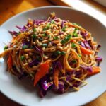 A plate of vibrant Thai Peanut Noodles with Crunchy Veggies, topped with chopped peanuts and green onions.
