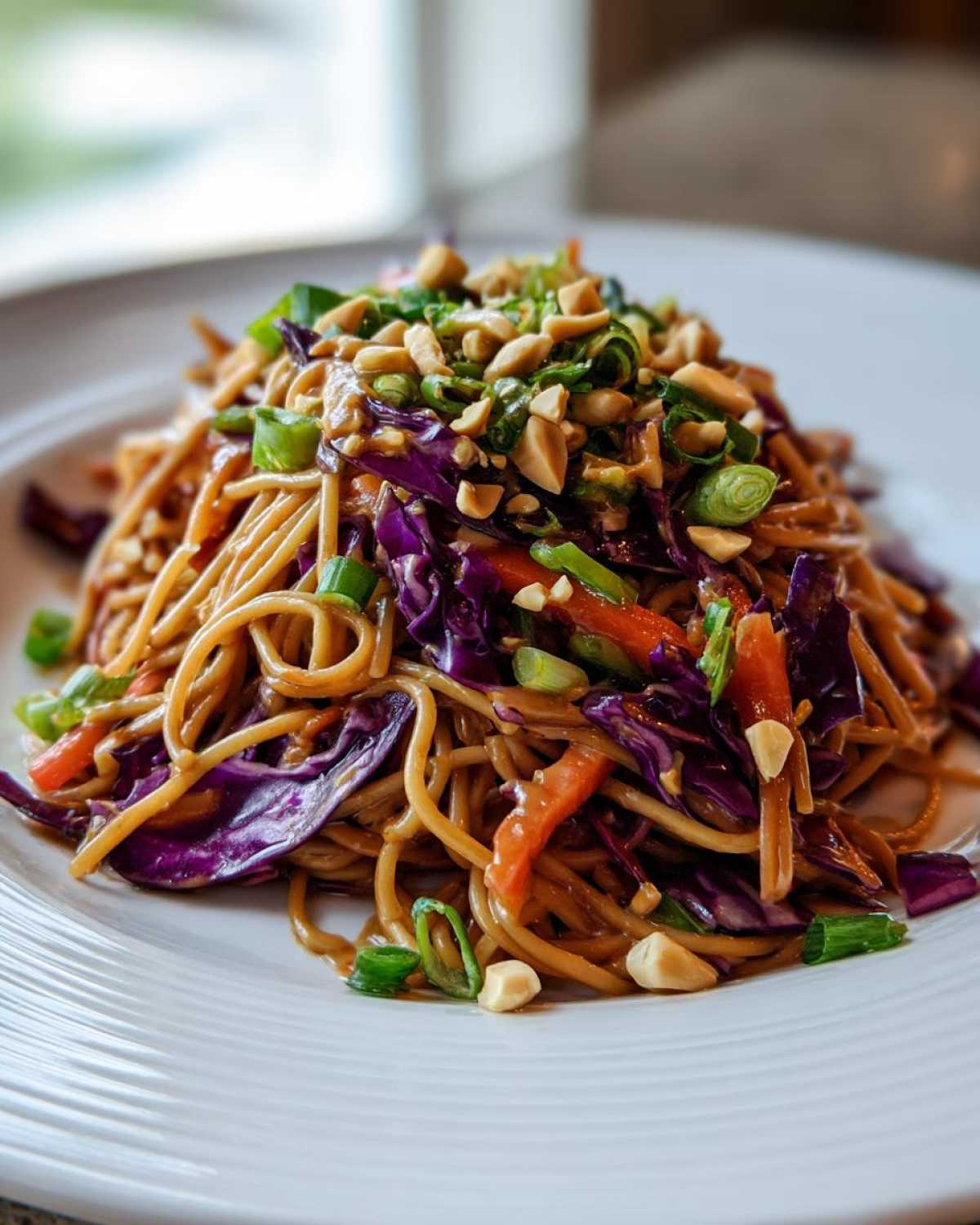 A close-up of a serving of Thai Peanut Noodles with Crunchy Veggies, topped with peanuts and green onions.