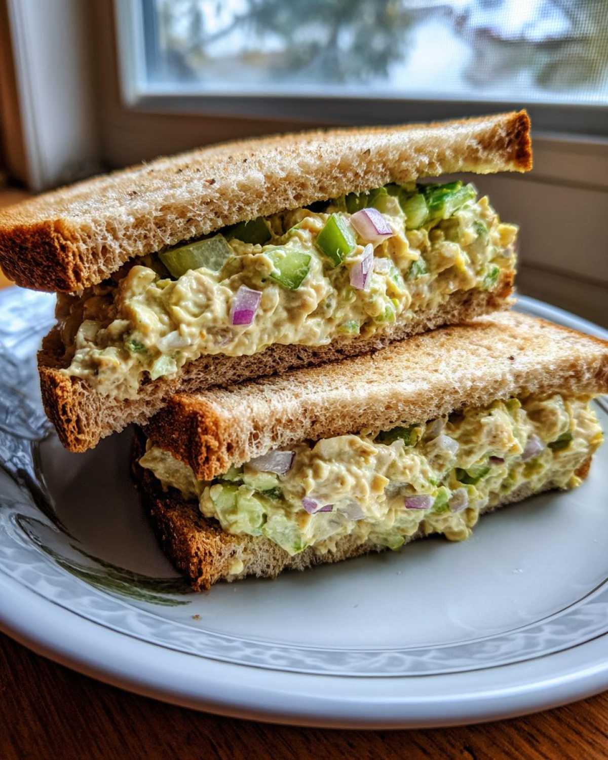 A halved Vegan Chickpea Salad Sandwich stacked on a plate, showing creamy filling with celery and red onion.
