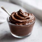 A close-up of rich, dark Vegan Chocolate Avocado Mousse swirled high in a small glass dish with a spoon.