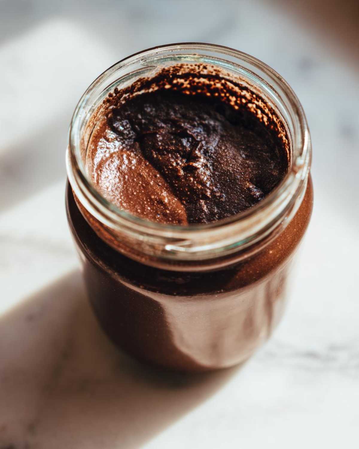 Overhead close-up of rich, dark Vegan Chocolate Chia Pudding set inside a clear glass jar.