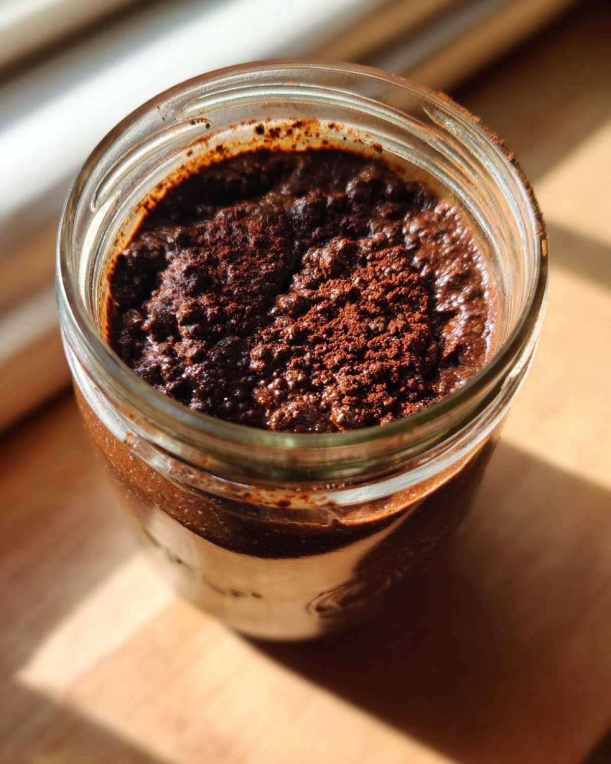 Overhead close-up of rich Vegan Chocolate Chia Pudding topped with cocoa powder in a glass jar.