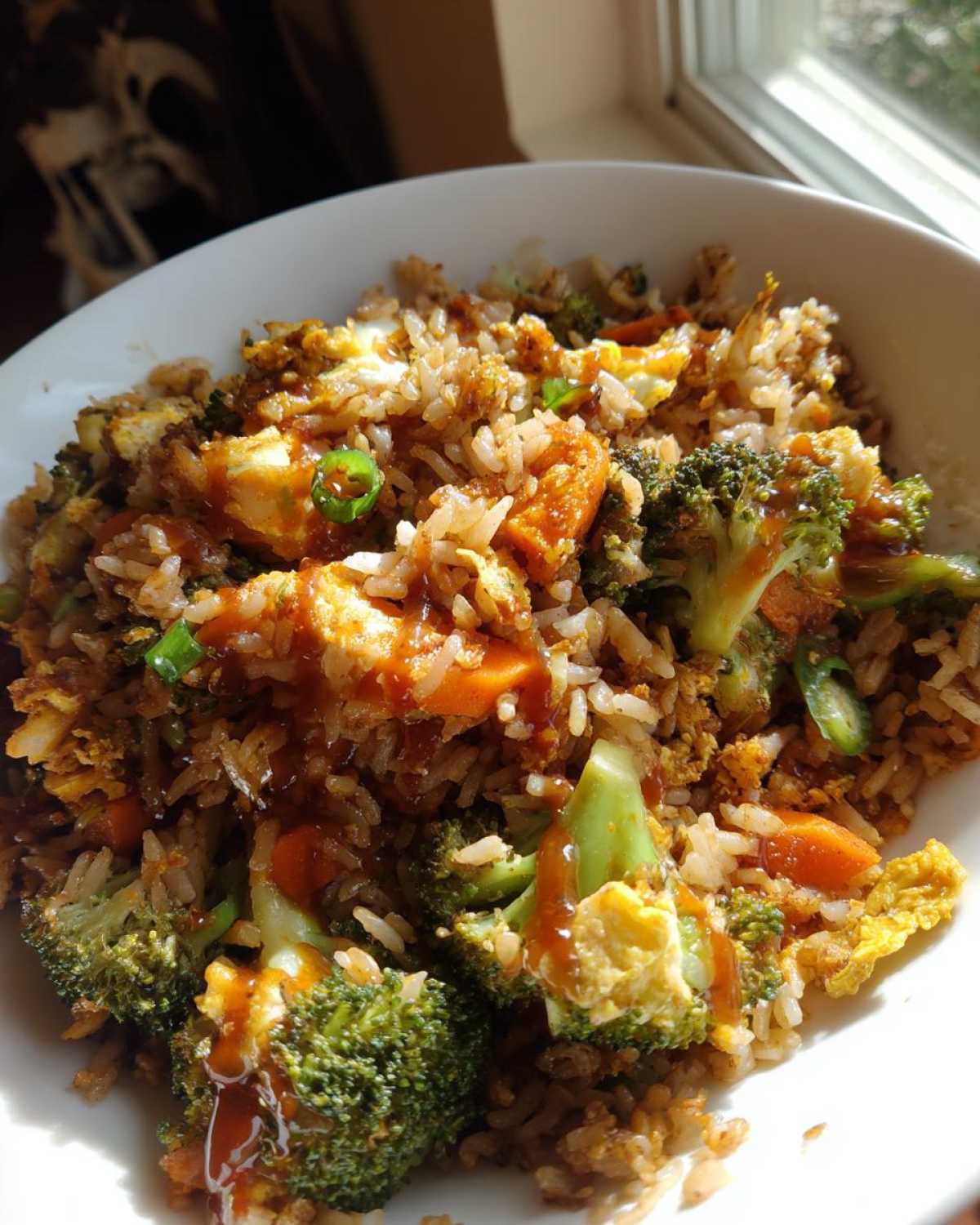 Close-up of Vegetable Fried Rice with broccoli, carrots, egg, and a drizzle of sesame ginger sauce in a white bowl.