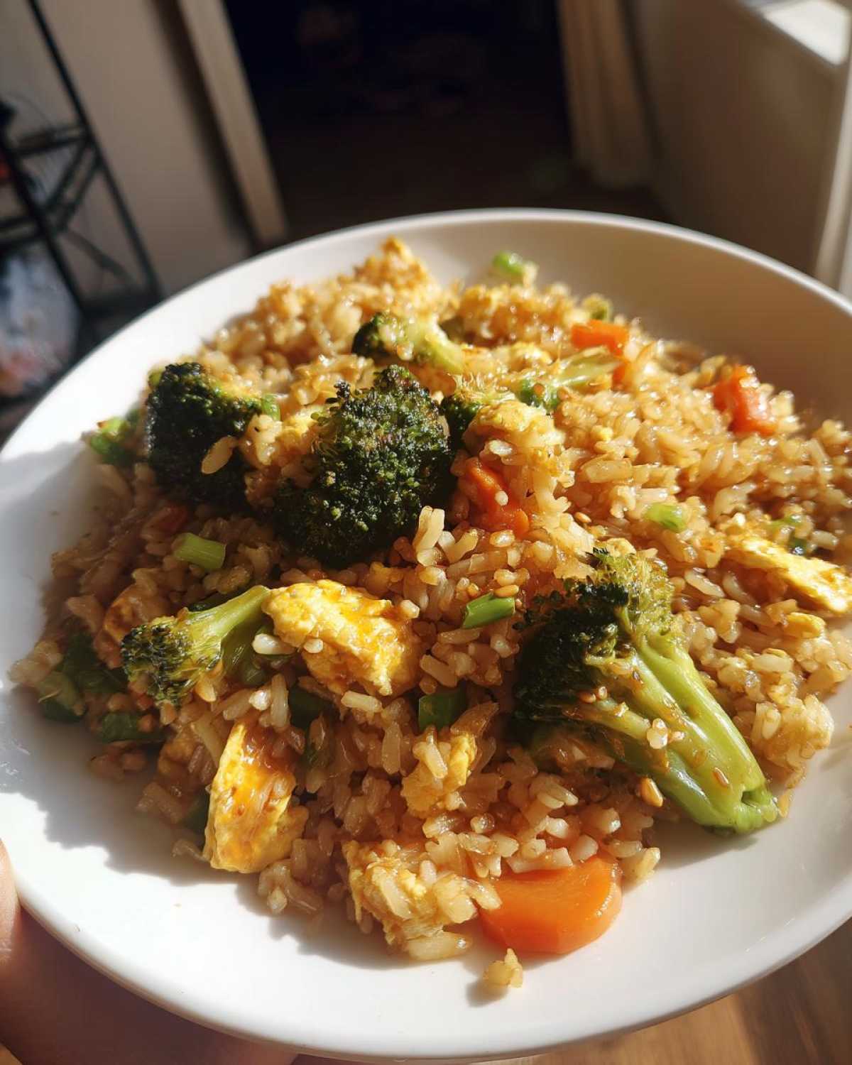 A close-up of a white bowl filled with Vegetable Fried Rice with Sesame Ginger Sauce, featuring broccoli, carrots, and scrambled egg.