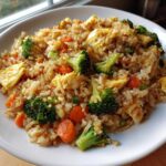 A close-up of flavorful Vegetable Fried Rice with Sesame Ginger Sauce, featuring bright green broccoli florets and orange carrots.