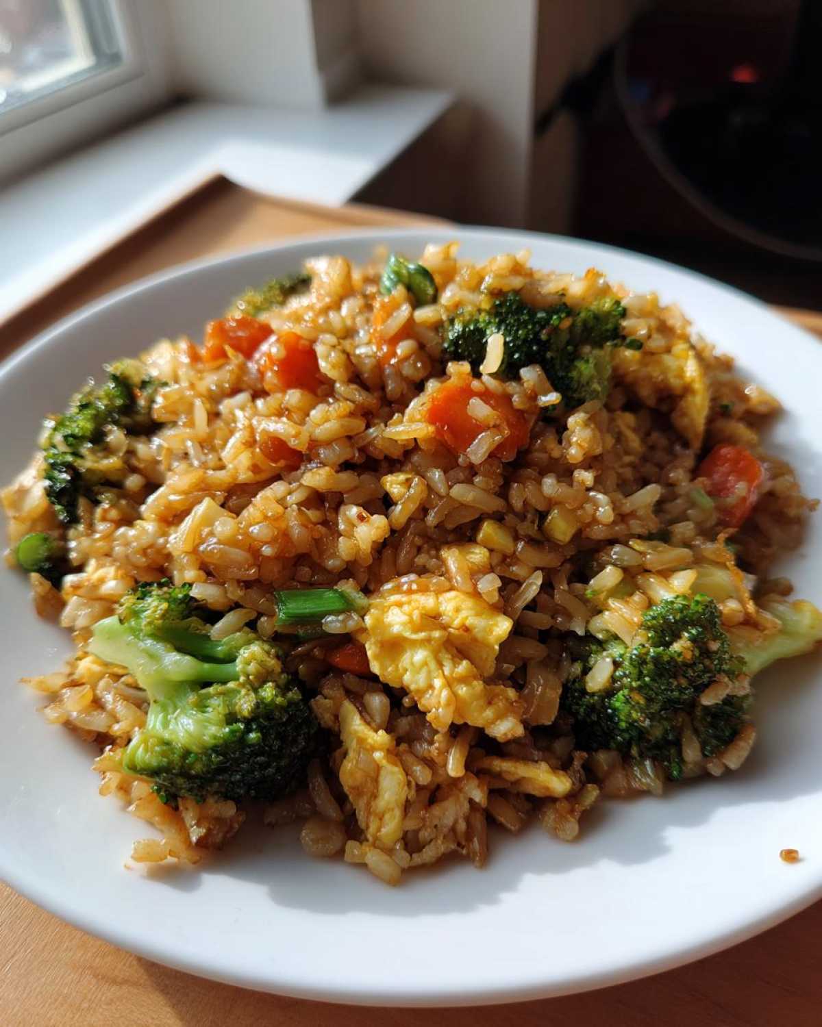 A close-up of a white plate piled high with Vegetable Fried Rice with Sesame Ginger Sauce, featuring broccoli and scrambled egg.