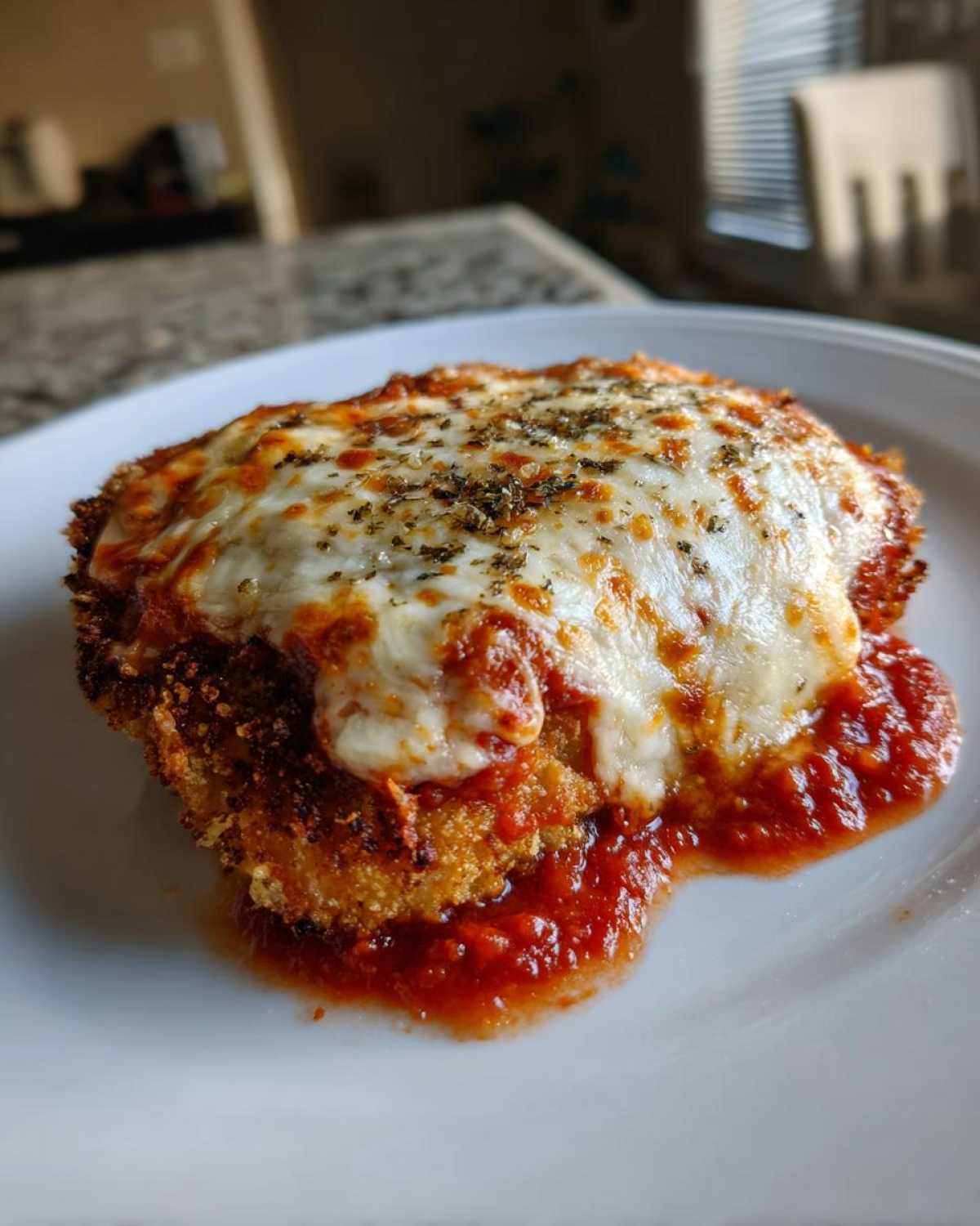 Close-up of a crispy Air Fryer Chicken Parmesan topped with melted mozzarella and herbs on a white plate.
