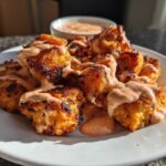 A plate piled high with crispy Air Fryer Salmon Bites generously drizzled with creamy Bang Bang Sauce.