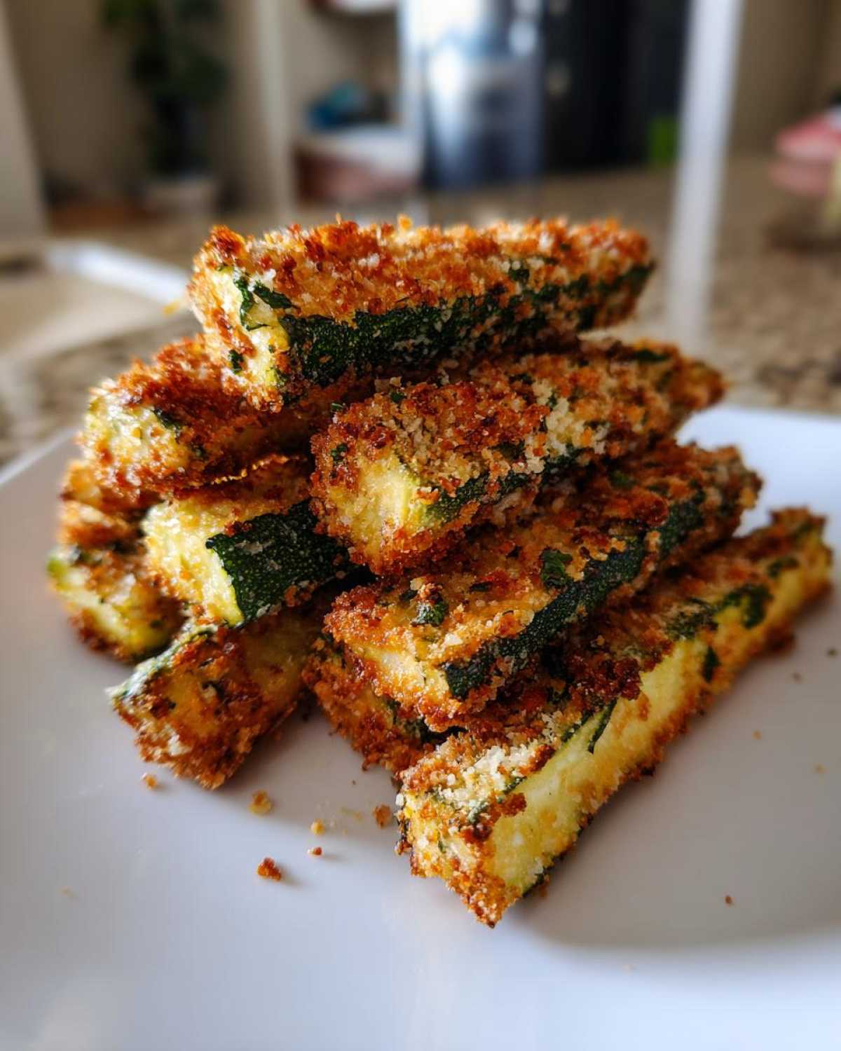 A stack of golden brown, crispy Air Fryer Zucchini Fries with Parmesan piled on a white plate.