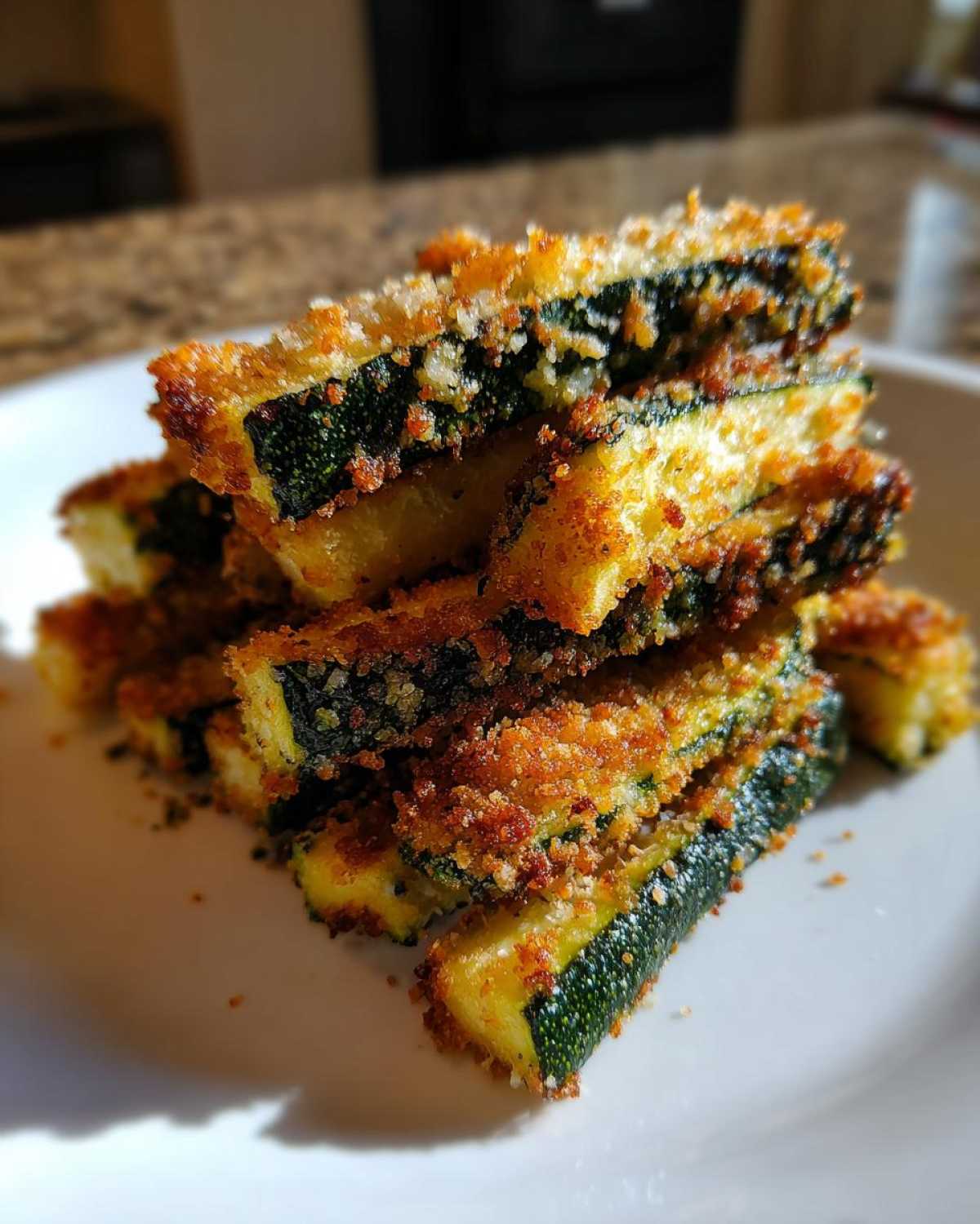 A stack of golden brown, crispy Air Fryer Zucchini Fries with Parmesan piled high on a white plate.