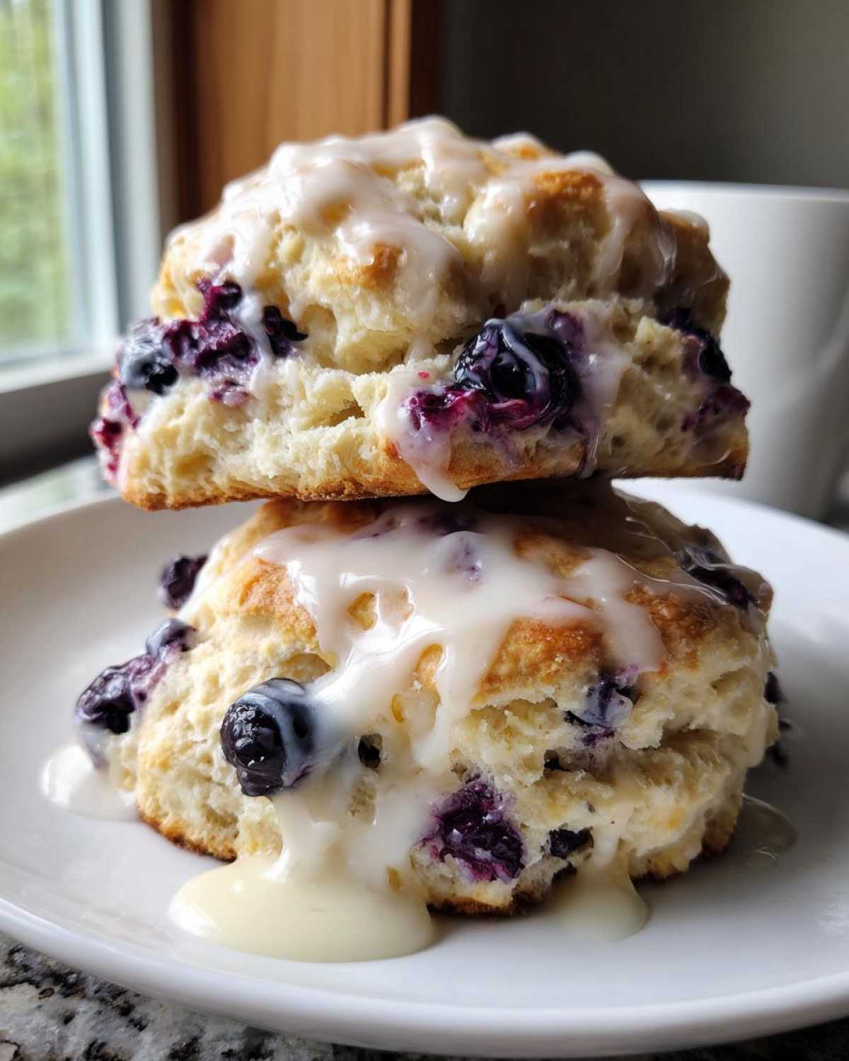 Two stacked, fluffy Blueberry Lemon Scones generously drizzled with a thick white lemon glaze.