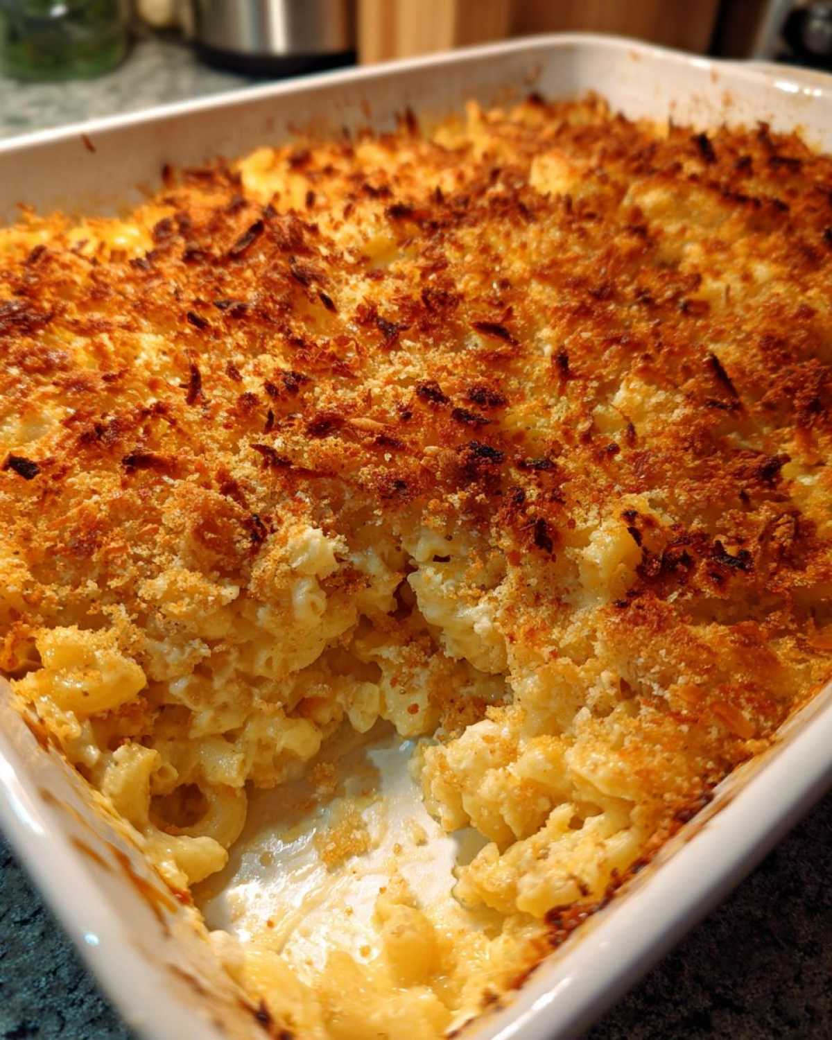 A close-up of Cheesy Baked Mac and Cheese with Crispy Top, showing a scoop removed from the white baking dish.