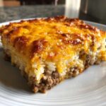 A thick slice of Cheesy Beef and Rice Casserole Comfort Dish with a browned, melted cheddar cheese topping.