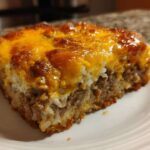 A square serving of Cheesy Beef and Rice Casserole Comfort Dish with a thick, bubbly, browned cheddar cheese topping.