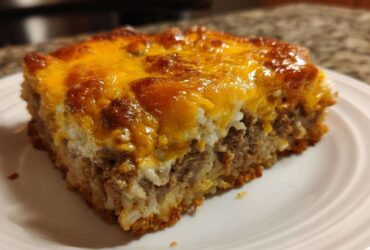 A square serving of Cheesy Beef and Rice Casserole Comfort Dish with a thick, bubbly, browned cheddar cheese topping.