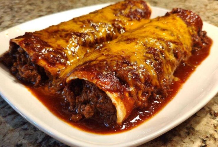 Two Cheesy Beef Enchiladas smothered in rich red sauce and melted cheddar cheese on a white plate.