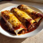 Three delicious Cheesy Beef Enchiladas covered in rich red sauce and melted golden cheese on a white plate.