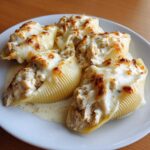 Four baked jumbo pasta shells filled with chicken and Alfredo sauce, topped with melted, browned cheese, representing Cheesy Chicken Alfredo Stuffed Shells.