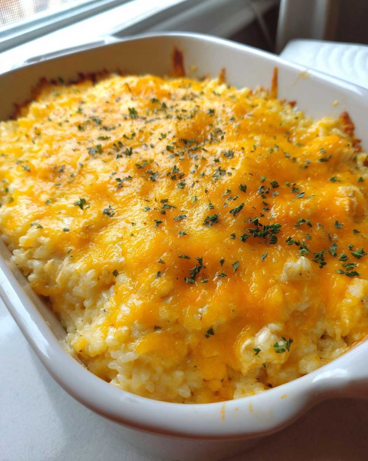 Close-up of a freshly baked Cheesy Chicken and Rice Casserole Easy Bake topped with melted cheddar and parsley.