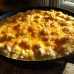 Close-up of a Cheesy Chicken and Rice Skillet in a cast iron pan, topped with melted cheddar cheese.