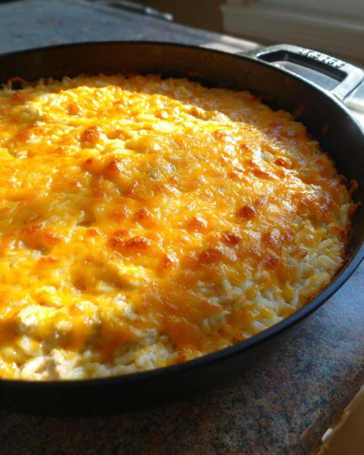 Close-up of a Cheesy Chicken and Rice Skillet with a thick, golden-brown layer of melted cheddar cheese on top.