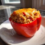 A single, bright red bell pepper stuffed with cheesy chicken and rice filling, baked until golden.