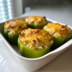 Four bright green bell peppers baked and filled with a cheesy chicken mixture, ready to serve.