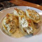 Four baked jumbo shells of Cheesy Chicken Stuffed Pasta with Cream Sauce, topped with melted cheese and herbs.