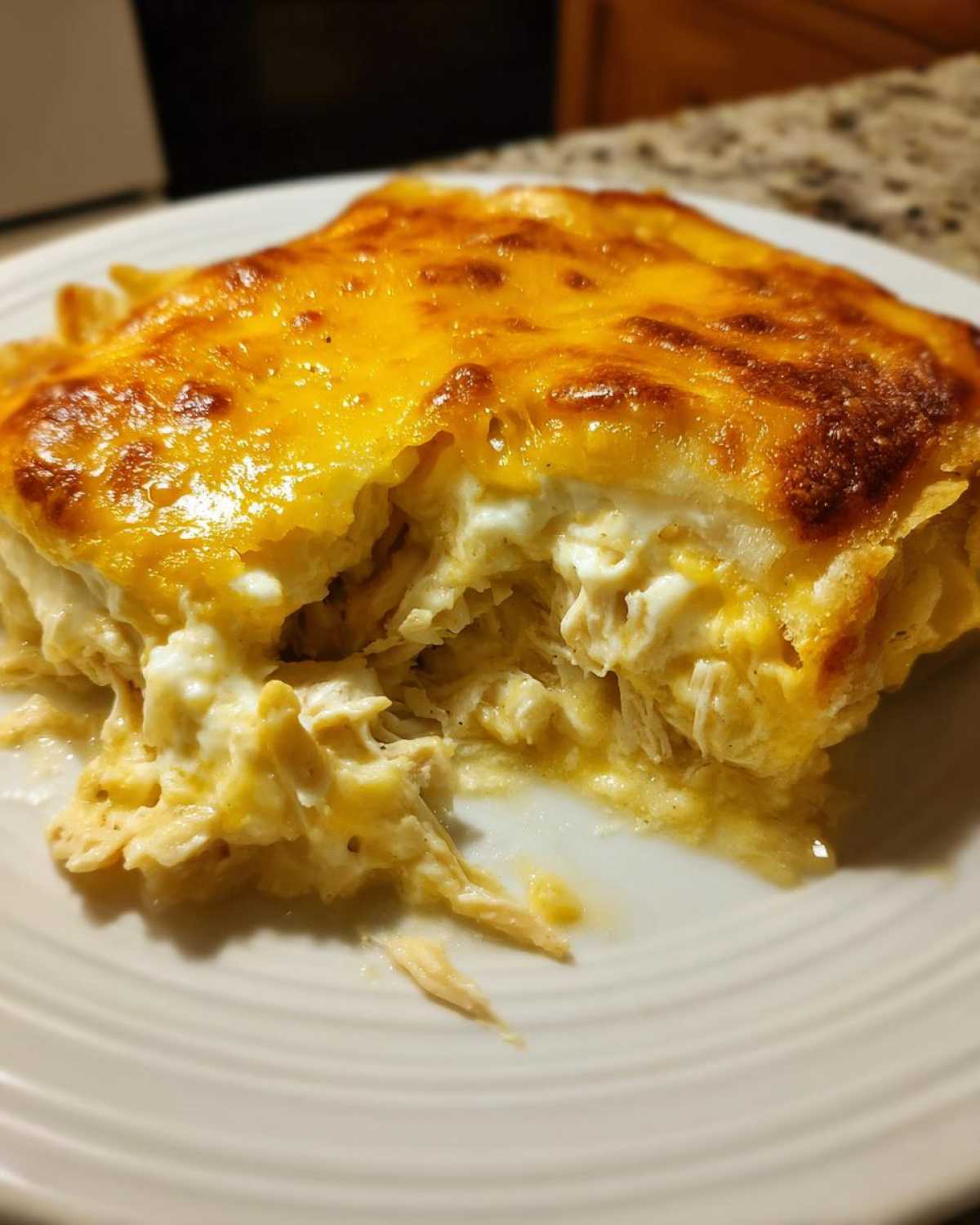A scoop of Cheesy Chicken Tortilla Bake showing shredded chicken and creamy sauce under a golden, melted cheese topping.
