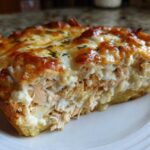 A close-up slice of Cheesy Chicken Tortilla Bake showing layers of shredded chicken, creamy sauce, and a bubbly, browned cheese topping.
