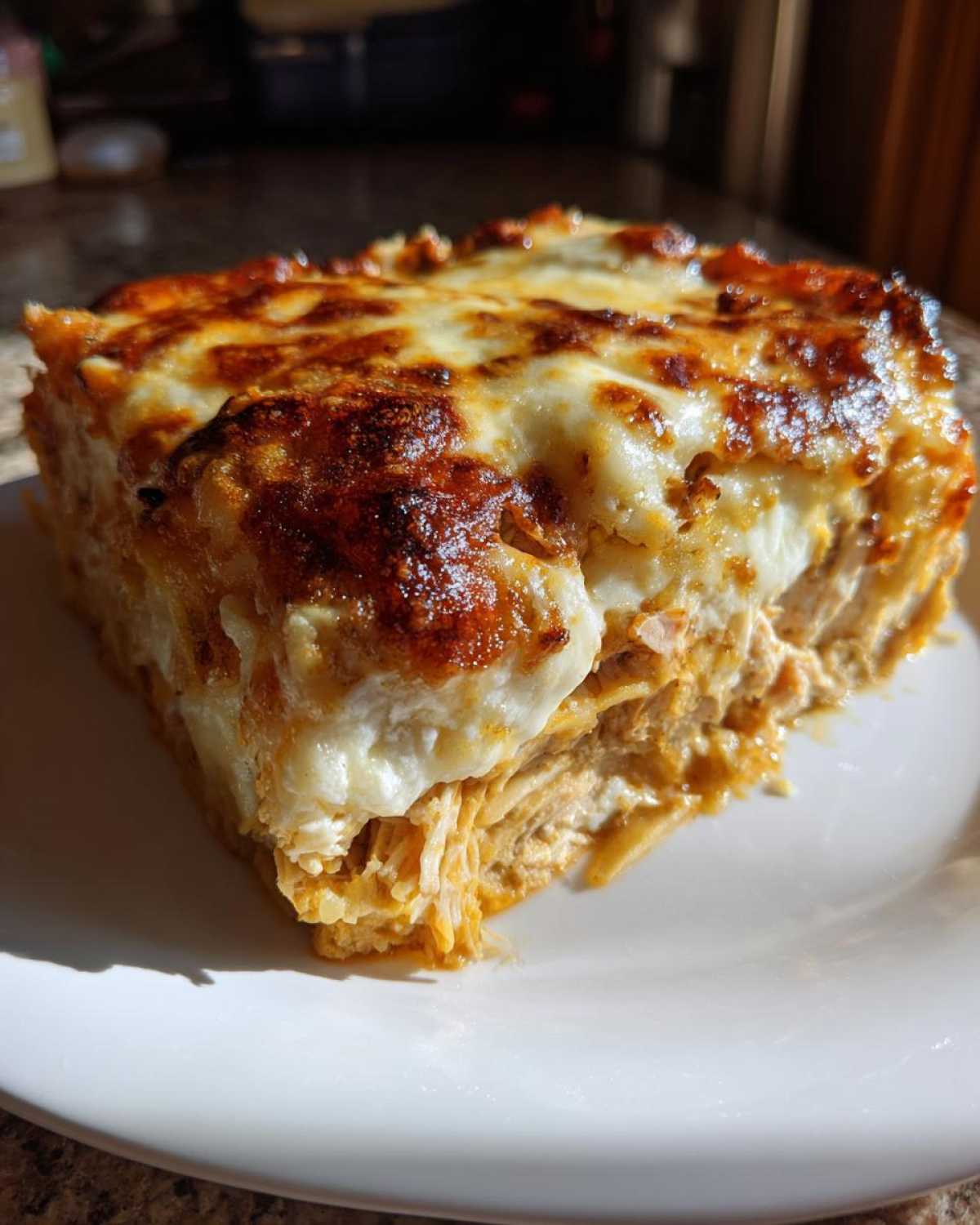 A generous slice of Cheesy Chicken Tortilla Bake showing layers of shredded chicken and a bubbly, browned cheese topping.