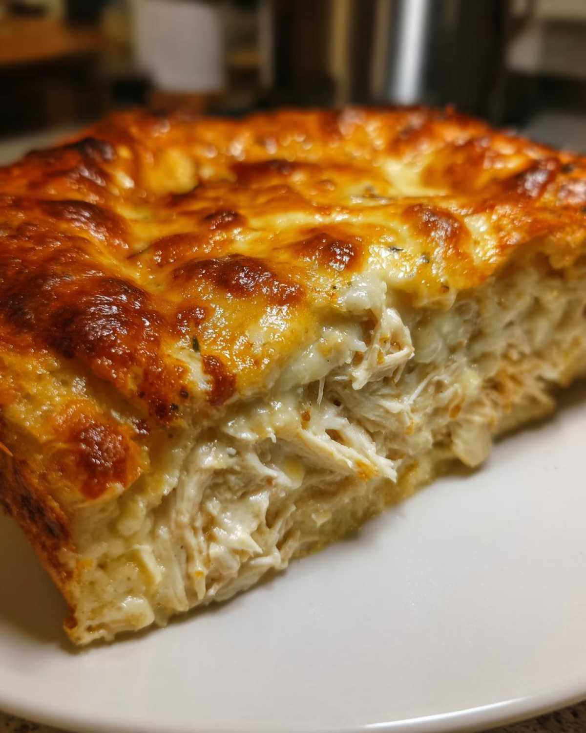Close-up of a slice of Cheesy Chicken Tortilla Bake showing shredded chicken filling and a bubbly, browned cheese topping.