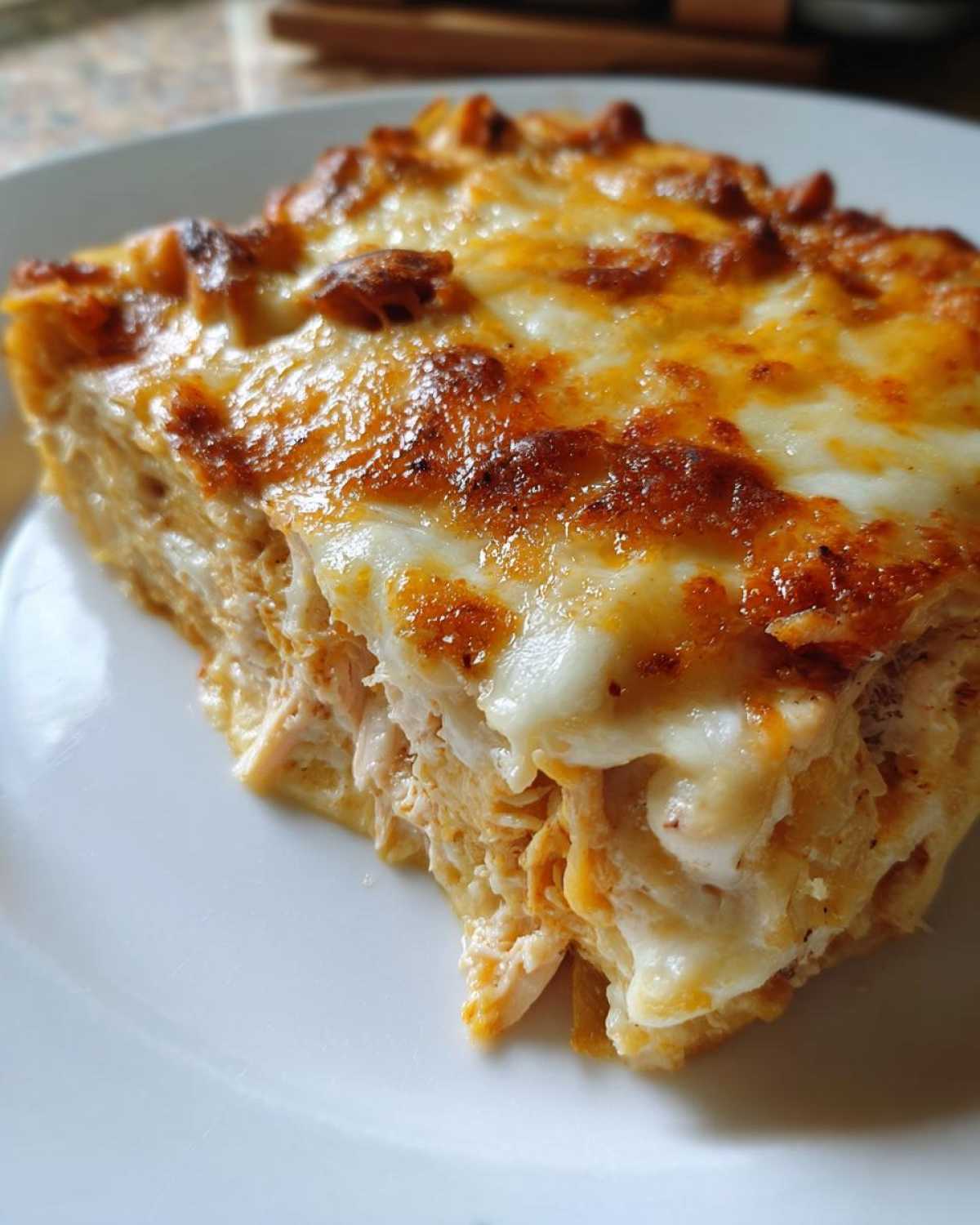 Close-up of a serving of Cheesy Chicken Tortilla Bake, showing layers of shredded chicken and a golden, bubbly cheese topping.