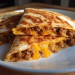 Two halves of a golden-brown Cheesy Ground Beef Quesadilla cut open to show melted cheese and seasoned ground beef filling.