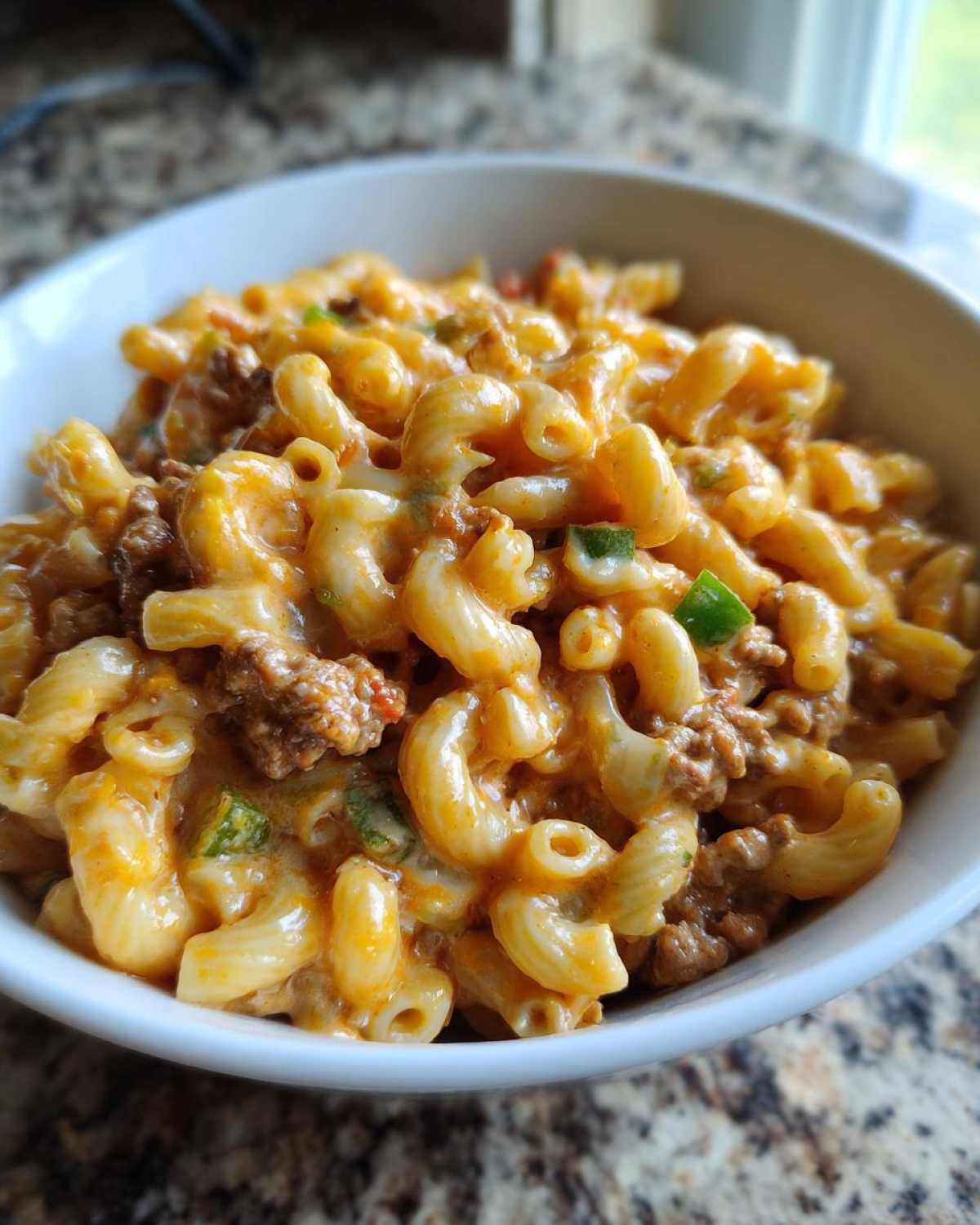 Close-up of a white bowl filled with creamy Cheesy Taco Pasta One Pot Dinner Idea, featuring elbow macaroni, ground meat, and green peppers.