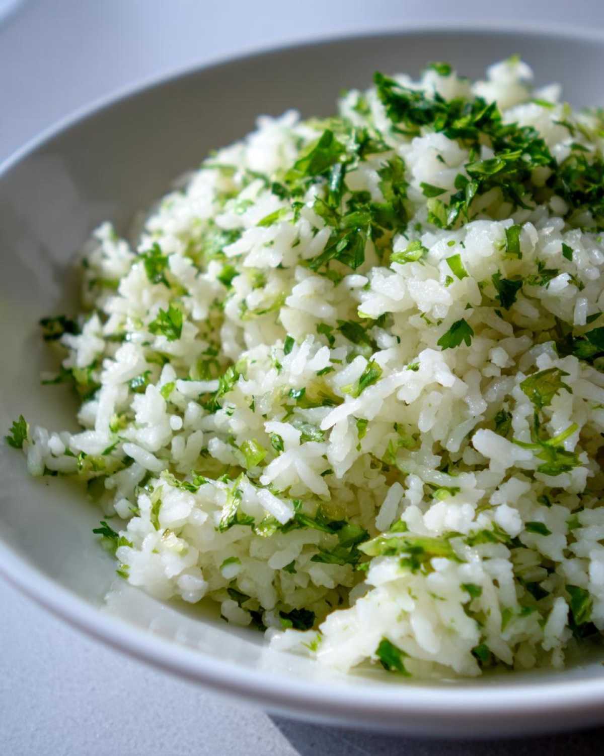 Close-up of fluffy Cilantro Lime Rice mixed with bright green herbs served in a white bowl.