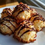 A close-up of golden-brown Coconut Macaroons with Dark Chocolate Drizzle piled on a white plate.