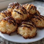 A stack of golden Coconut Macaroons with Dark Chocolate Drizzle served on a white plate.