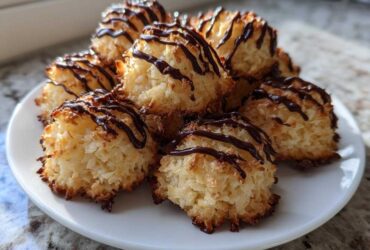 A stack of golden Coconut Macaroons with Dark Chocolate Drizzle served on a white plate.