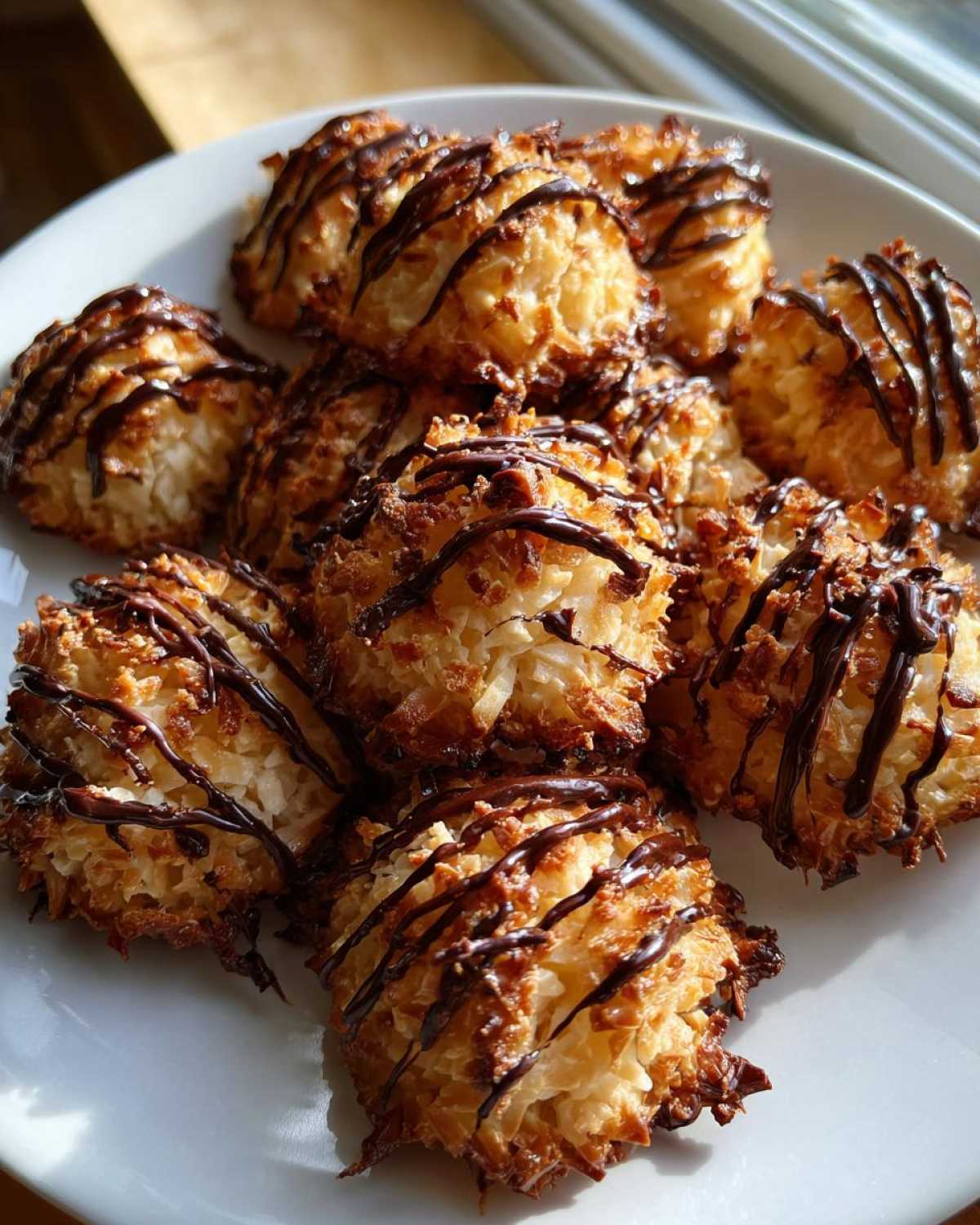 A plate of golden brown Coconut Macaroons with Dark Chocolate Drizzle stacked together.