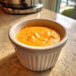 A close-up of thick, orange Copycat Raising Cane’s Sauce served in a small white fluted ramekin.
