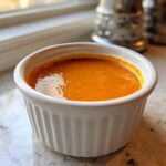 A close-up of bright orange Copycat Raising Cane’s Sauce served in a small, white, fluted ramekin.
