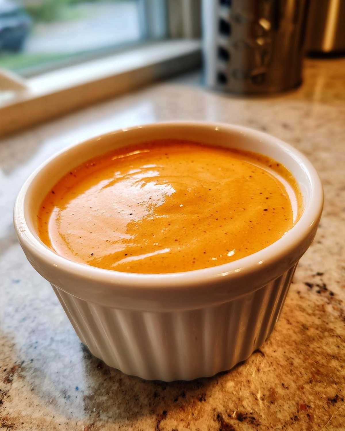 A close-up shot of creamy, orange-hued Copycat Raising Cane’s Sauce served in a small white fluted ramekin.