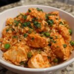 A white bowl filled with Creamy Cajun Chicken and Rice Skillet, featuring chunks of chicken, rice, and green peas, topped with parsley.